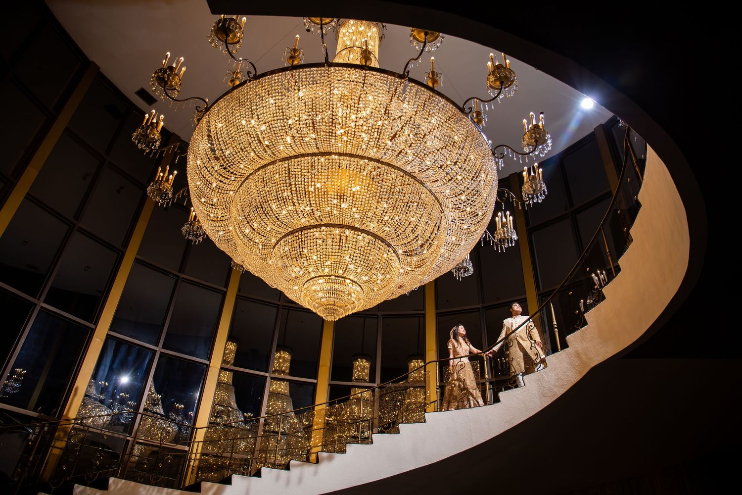 Indian wedding couple descends the grand staircase beneath a stunning crystal chandelier at night, Xenia Helix Photography, Boston, MA