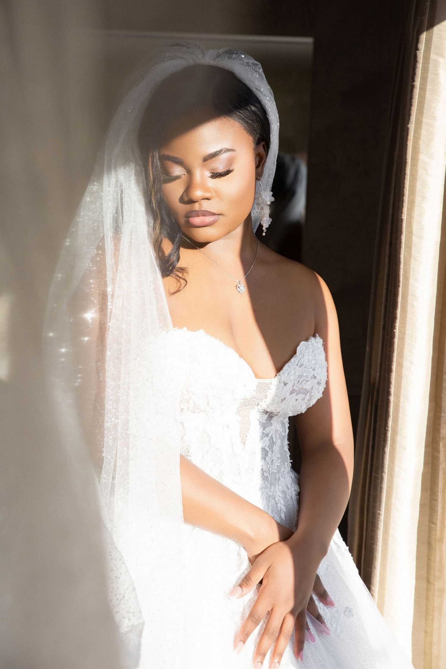 Elegant bride in lace gown and veil poses in soft window light with eyes closed, Independence Harbor, Assonet, MA