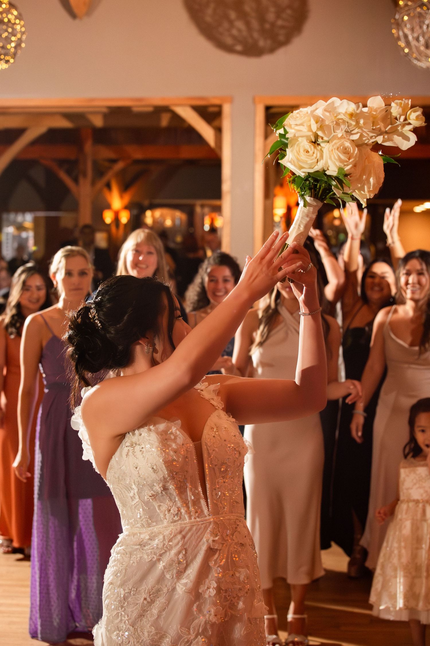 Bride in a lace gown tossing her white orchid bouquet to excited guests at the wedding reception, Harrington Farm, Princeton, MA