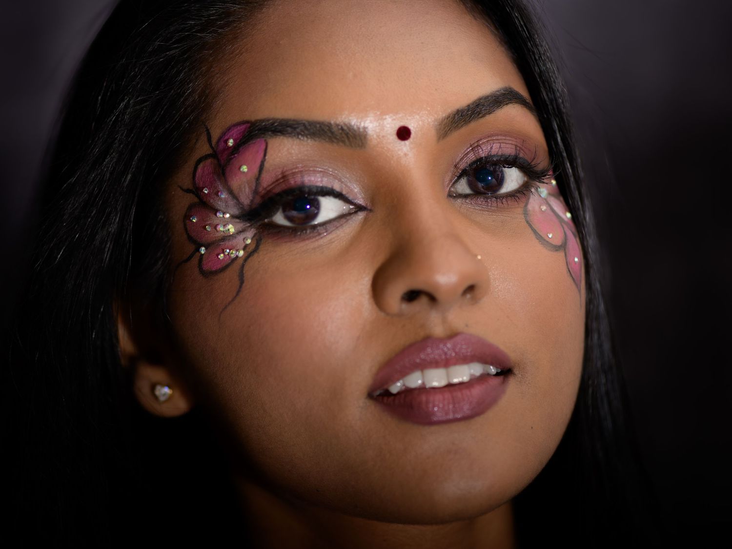 Young woman with decorative butterfly face art, bindi, and elegant makeup in a professional portrait.