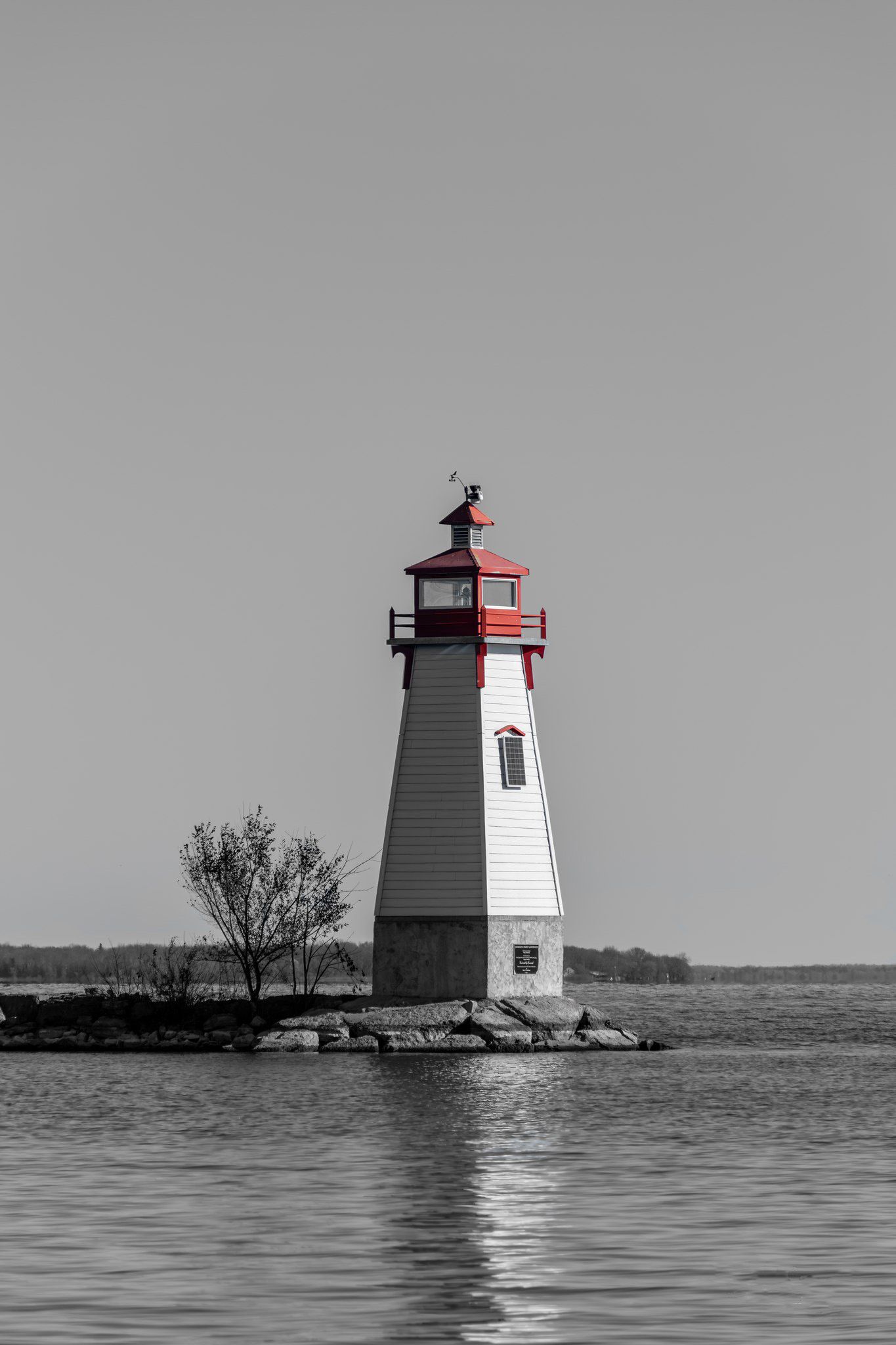 Black and white photo of a red-topped lighthouse on a rocky shoreline surrounded by calm water.