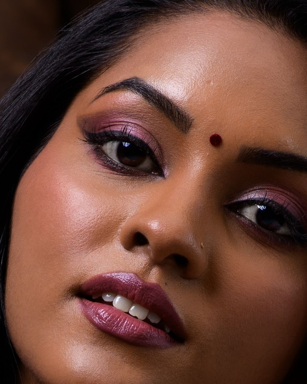 Close-up portrait of a South Asian woman with bold burgundy eye makeup, bindi, and matching lip color.