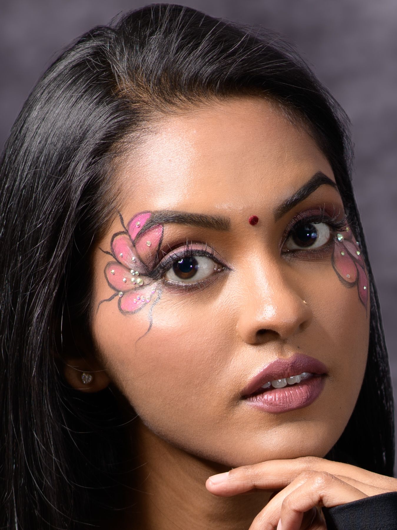 Woman with butterfly face paint and jewel accents, wearing pink eye makeup and a bindi.