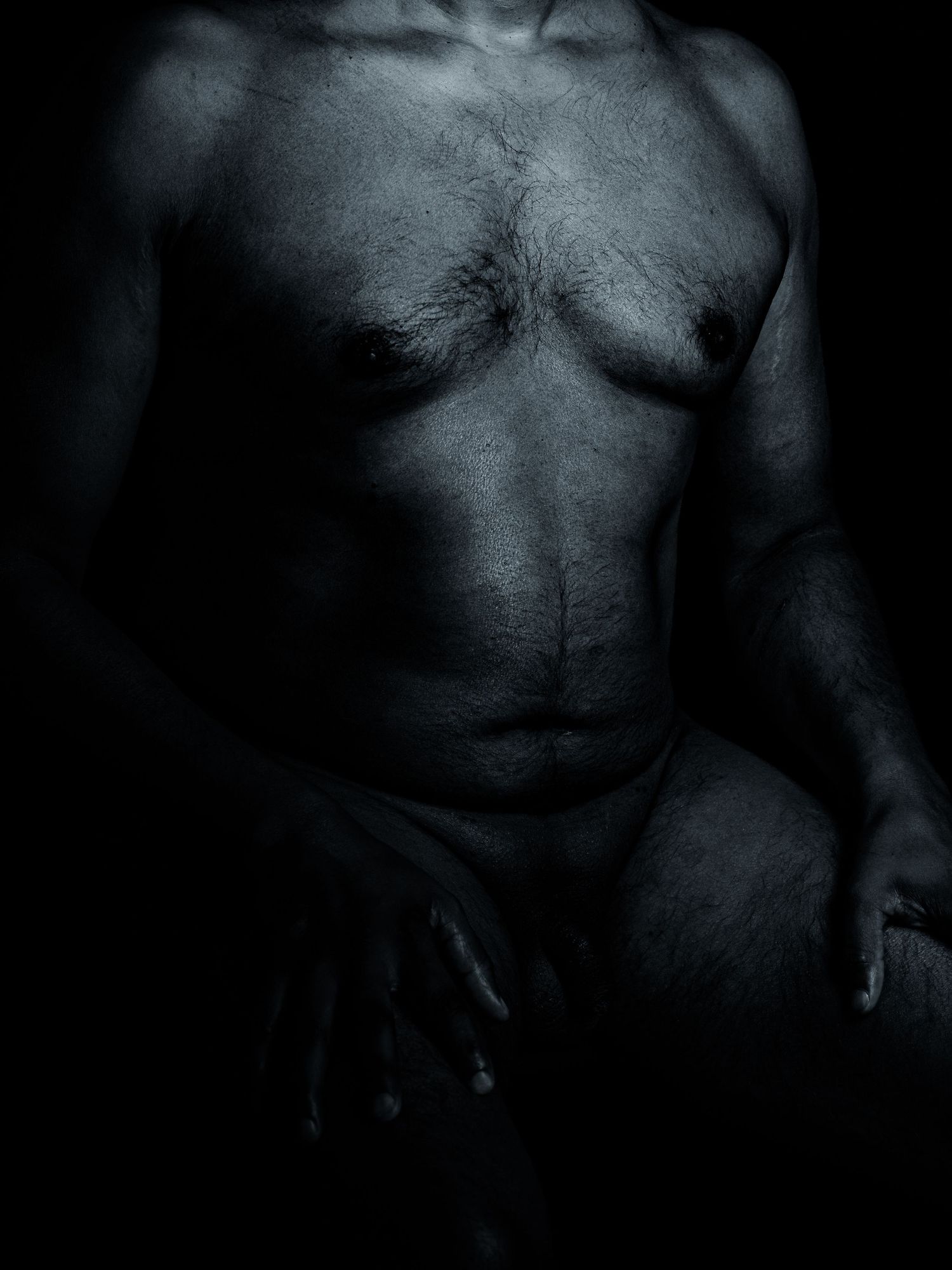Dark artistic black and white photo of a male torso with dramatic chiaroscuro lighting highlighting muscular form.
