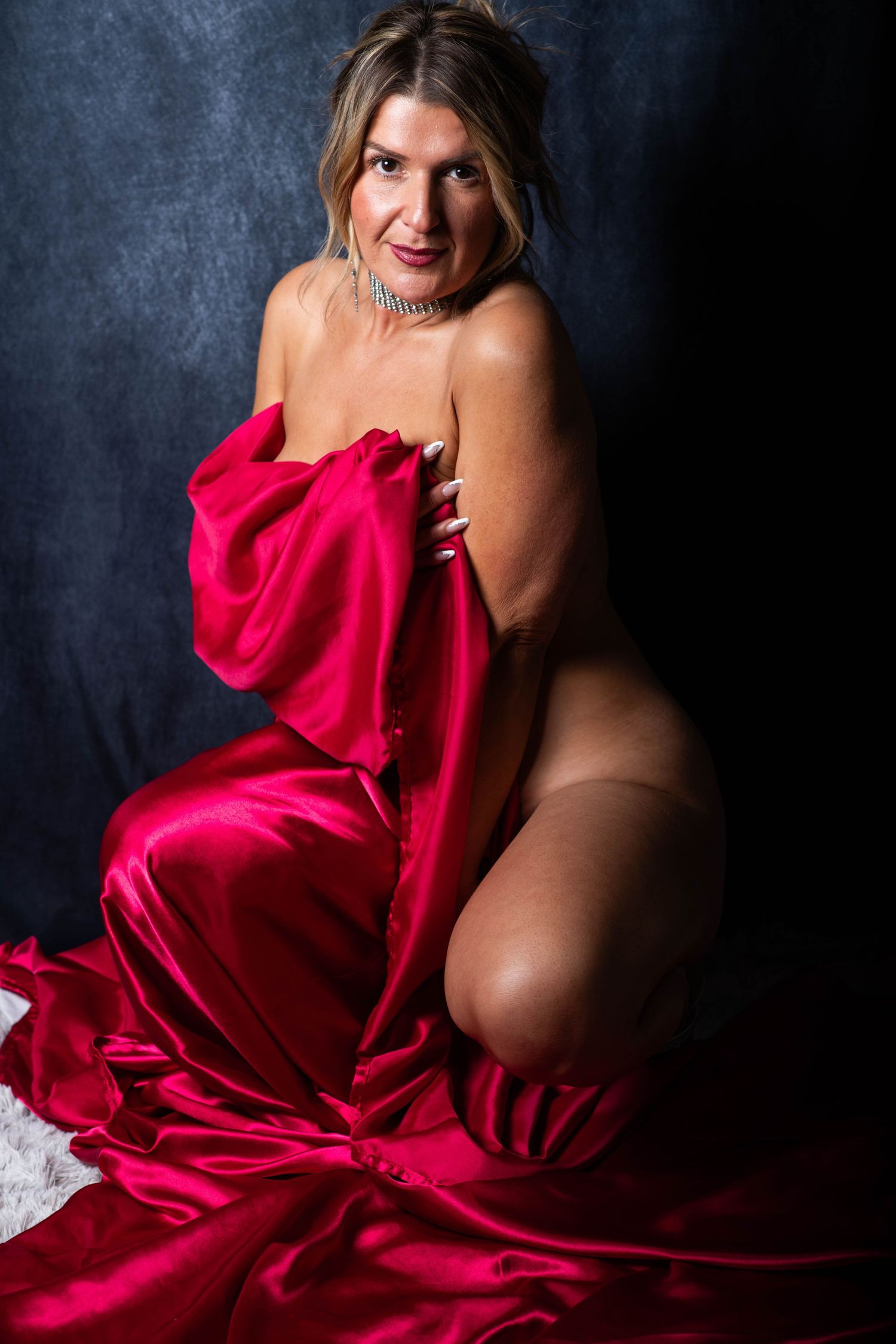 Woman posing with red satin fabric in dramatic studio portrait photography.