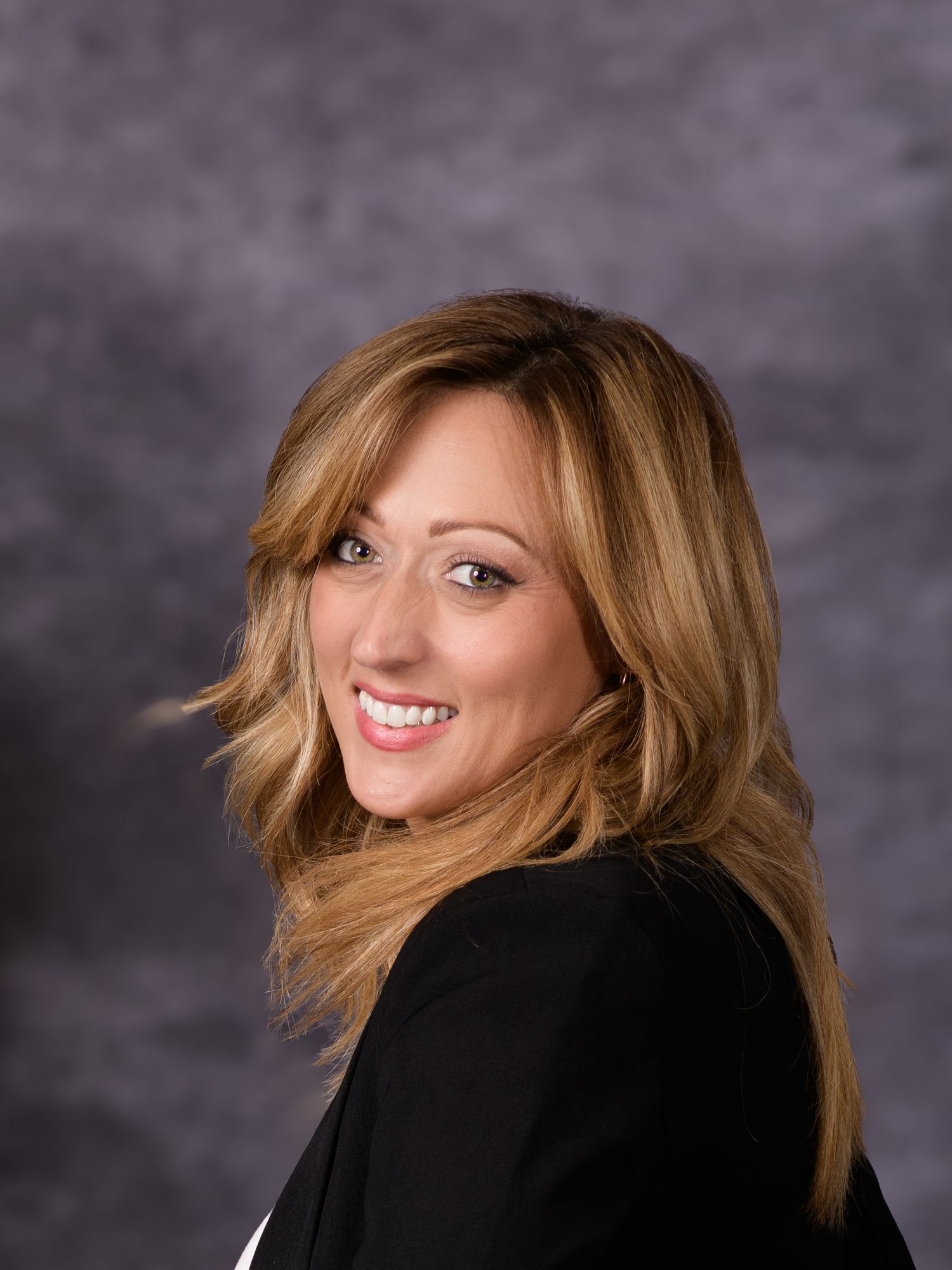 Professional portrait of a smiling blonde woman in a black top against a gray studio background.