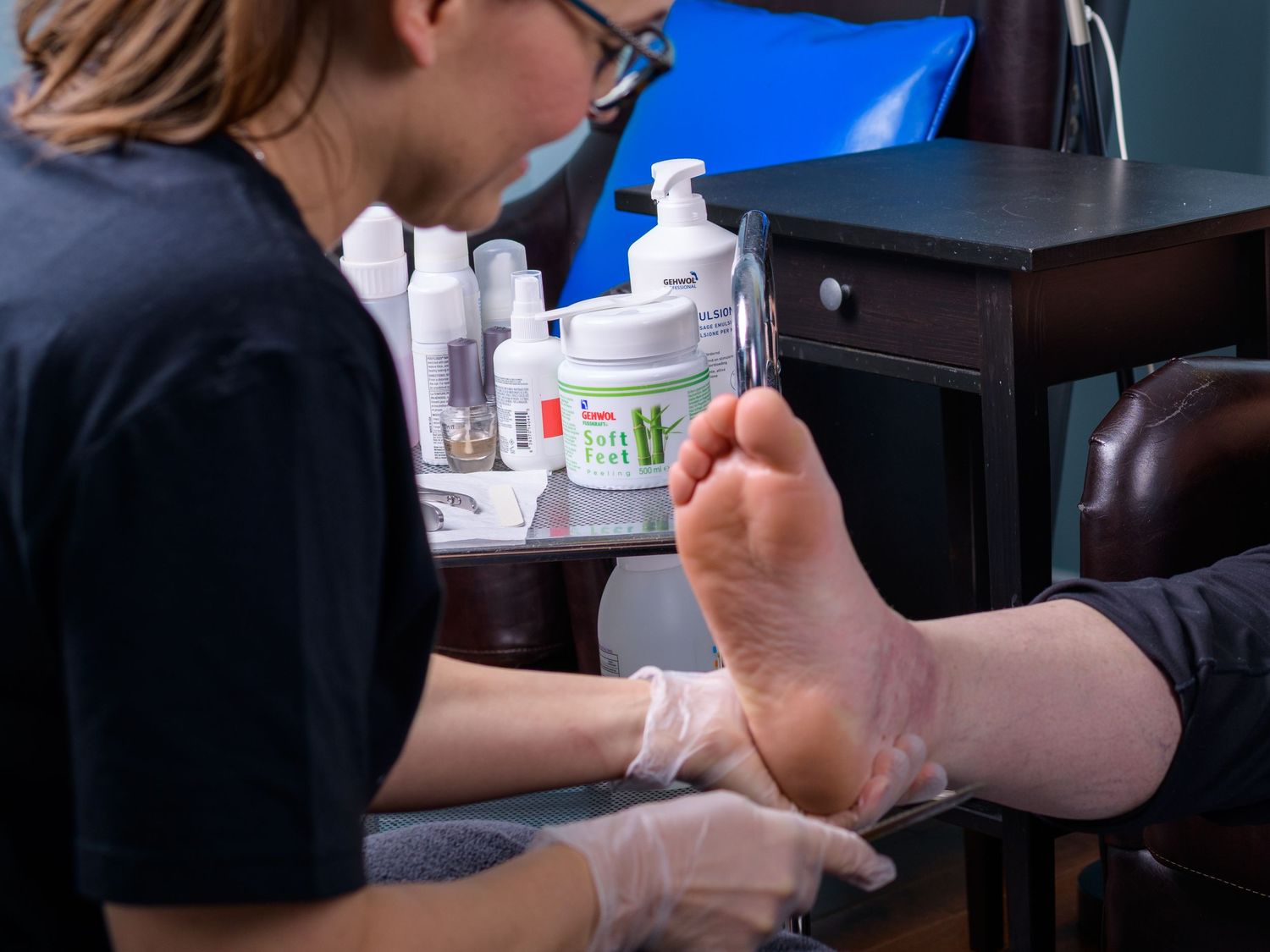 Nail technician wearing gloves carefully examines and treats a client's foot during a professional pedicure service.