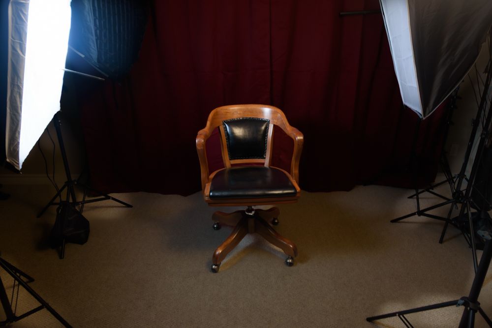 Professional photography studio setup with lighting equipment, backdrop stands, and a wooden chair arranged for a shoot.