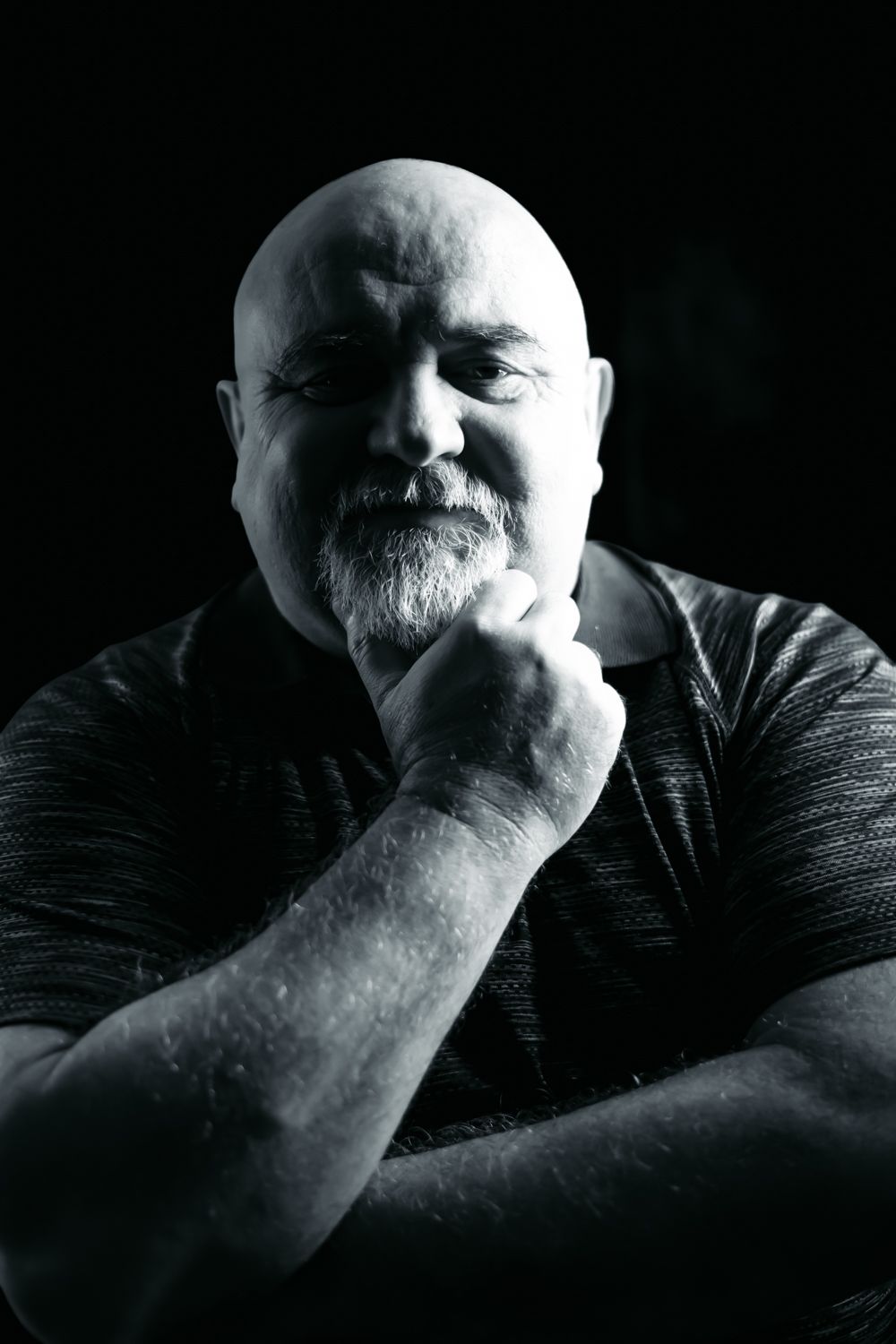 Black and white close up of a man resting his chin on his hand, looking thoughtfully into the camera with soft, detailed lighting.