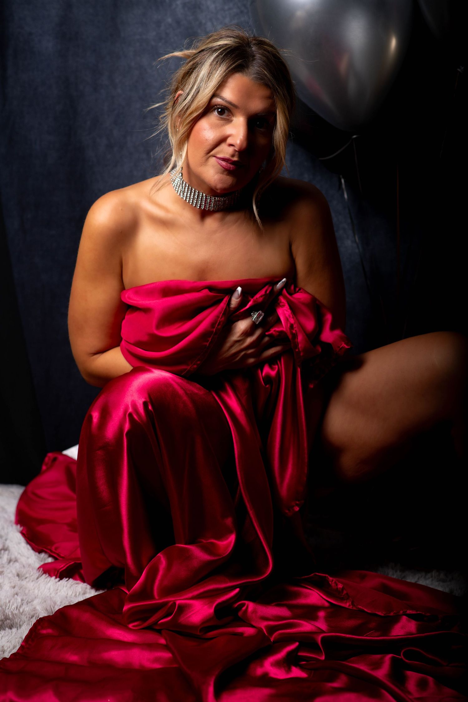 A figure draped in flowing red satin fabric poses dramatically against a dark background in an artistic portrait series.