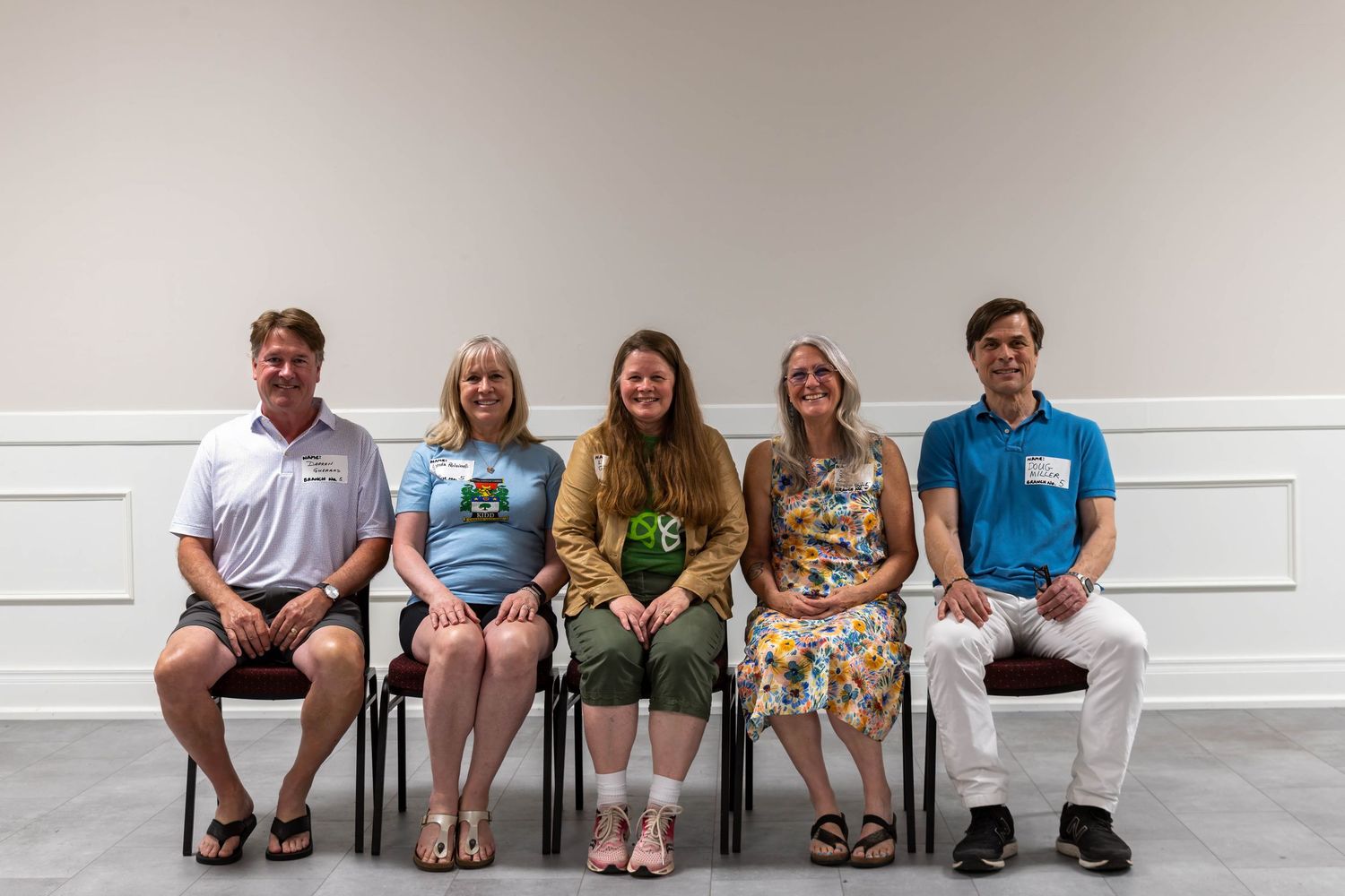 Five people sitting in chairs smiling for a group portrait photo in a bright white room.