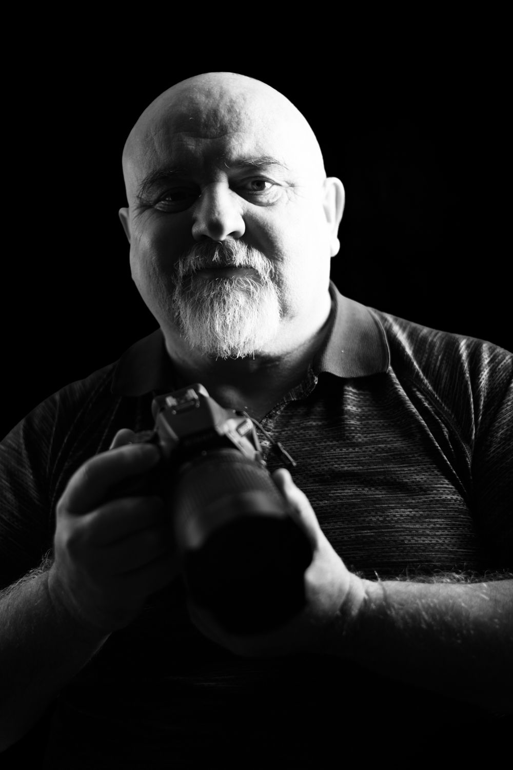 A photographer holding a professional camera in a moody black and white setting, symbolizing the bridge between creator and subject.