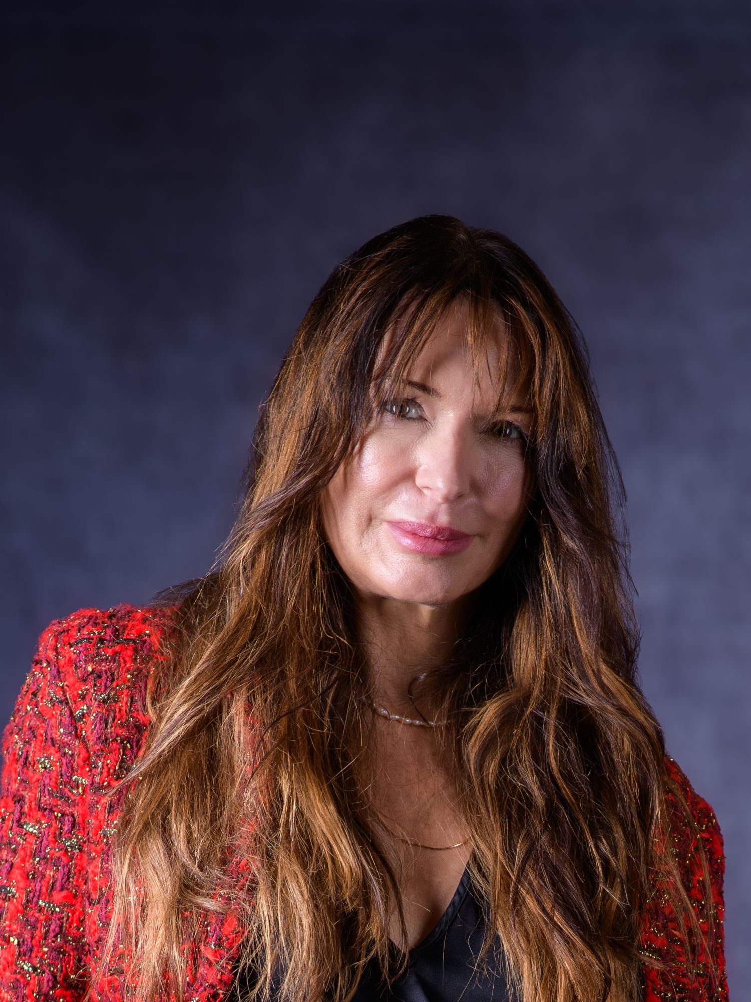 Woman with long brunette hair wearing a red tweed blazer poses for a professional portrait photo.
