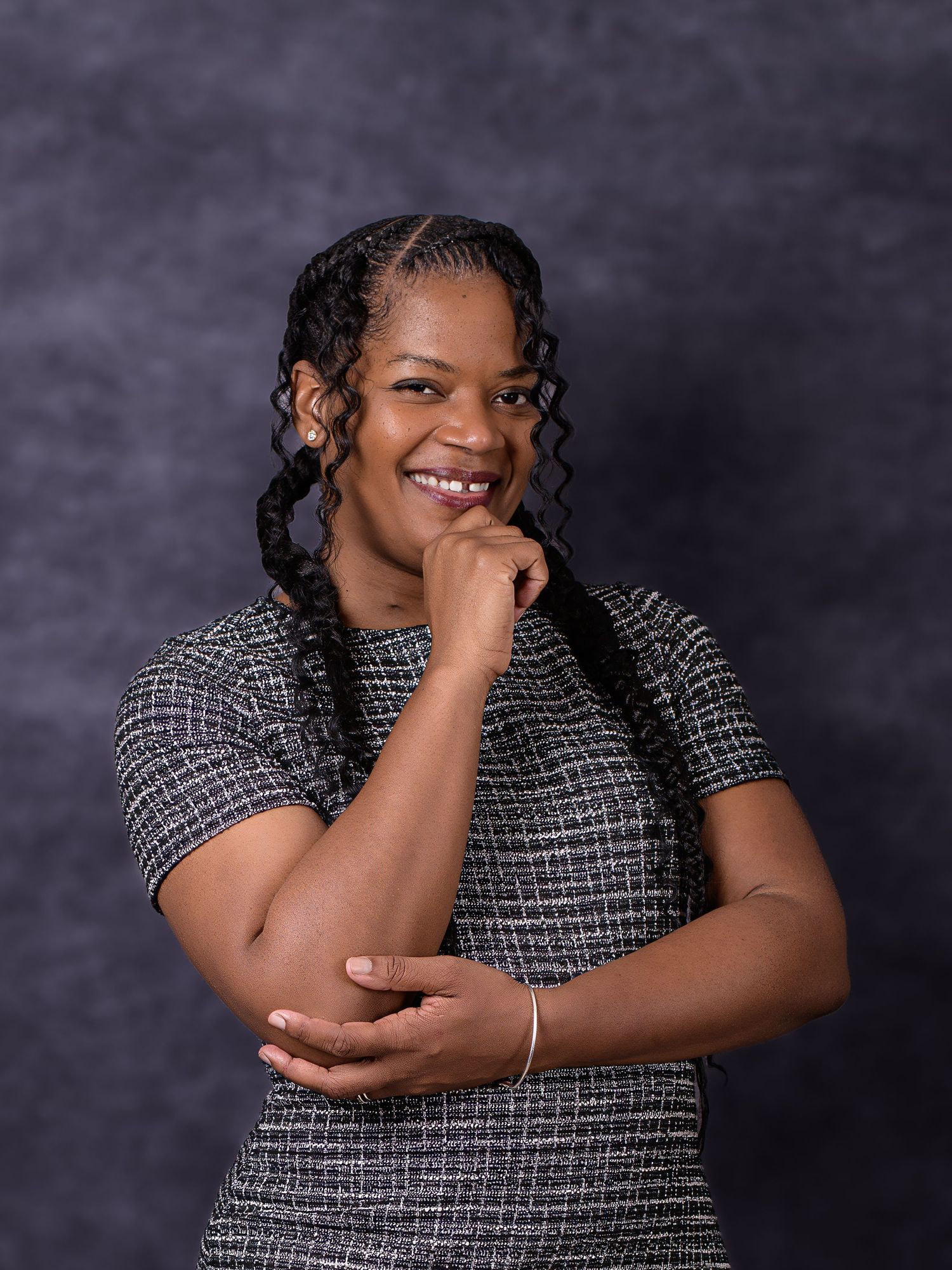 Smiling young woman with braided hair poses confidently in a gray tweed top against a dark studio background.