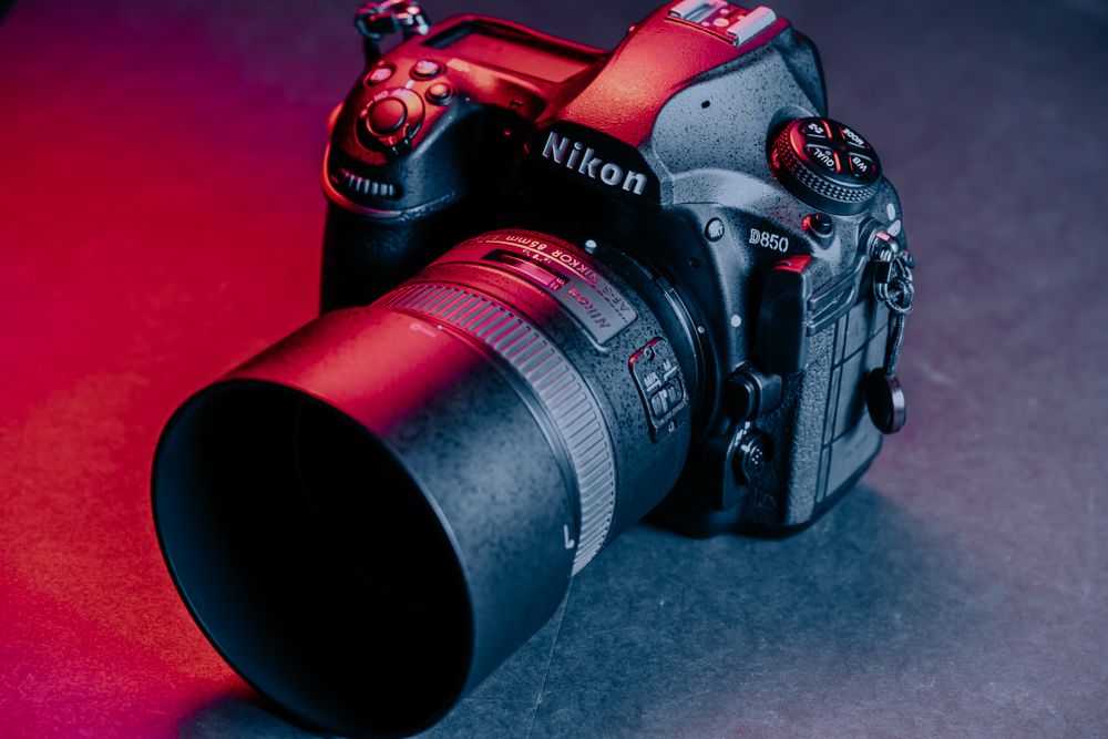 Professional NikonD850 DSLR camera with red lens hood against dark background with dramatic lighting.
