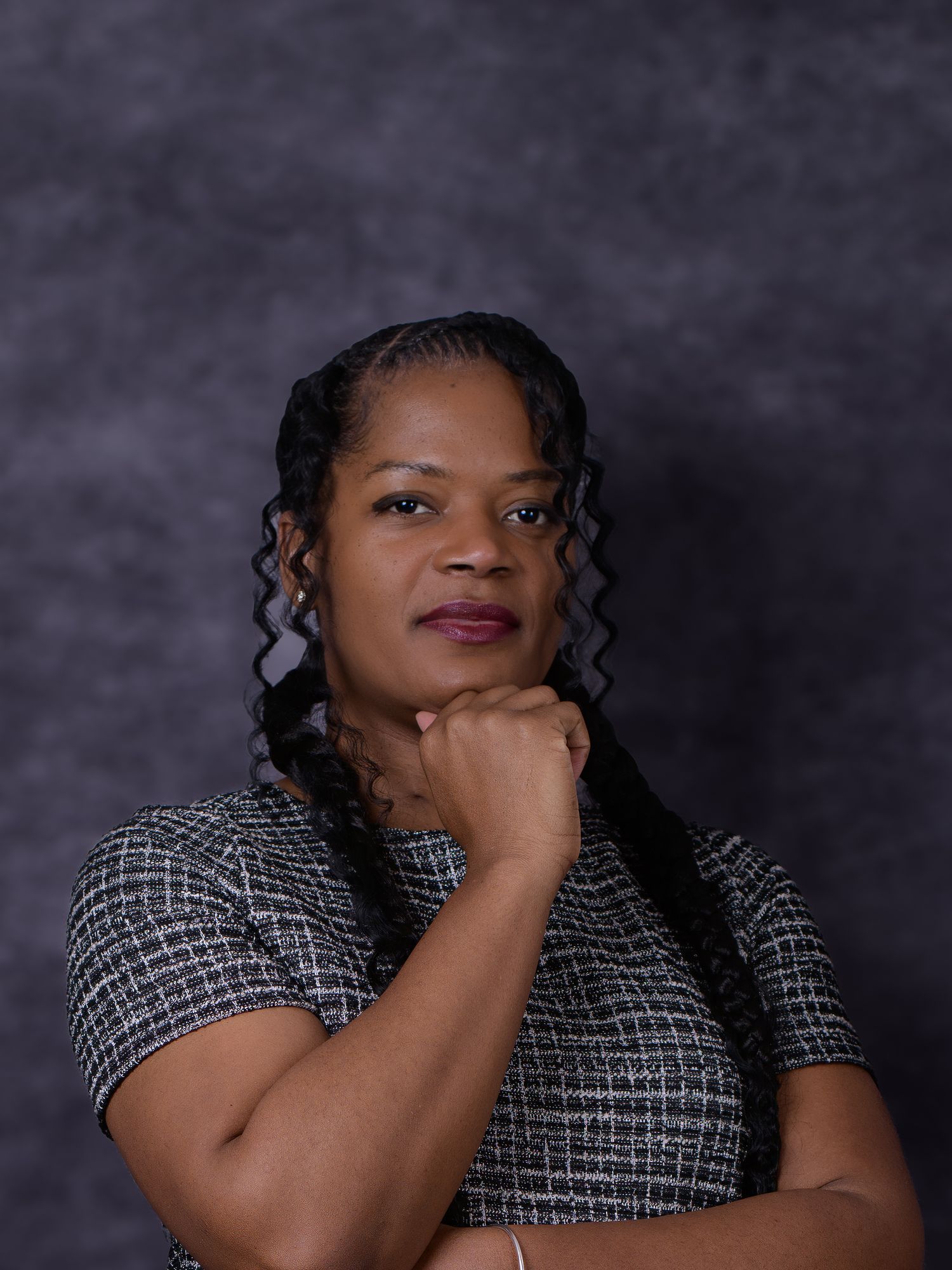 Professional woman with braided hair in a tweed dress, posing confidently against a gray studio background.