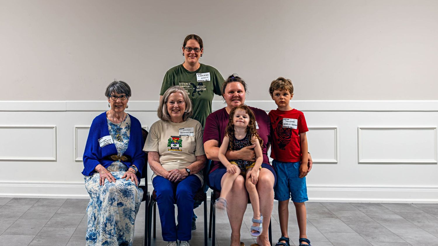 Group of six people, including children and elderly, posing together for a family portrait in a bright indoor setting.