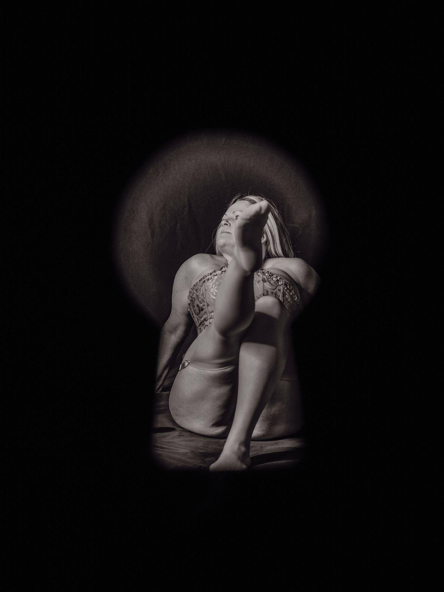Black and white photo of a tattooed person curled up, viewed through a keyhole-shaped vignette.