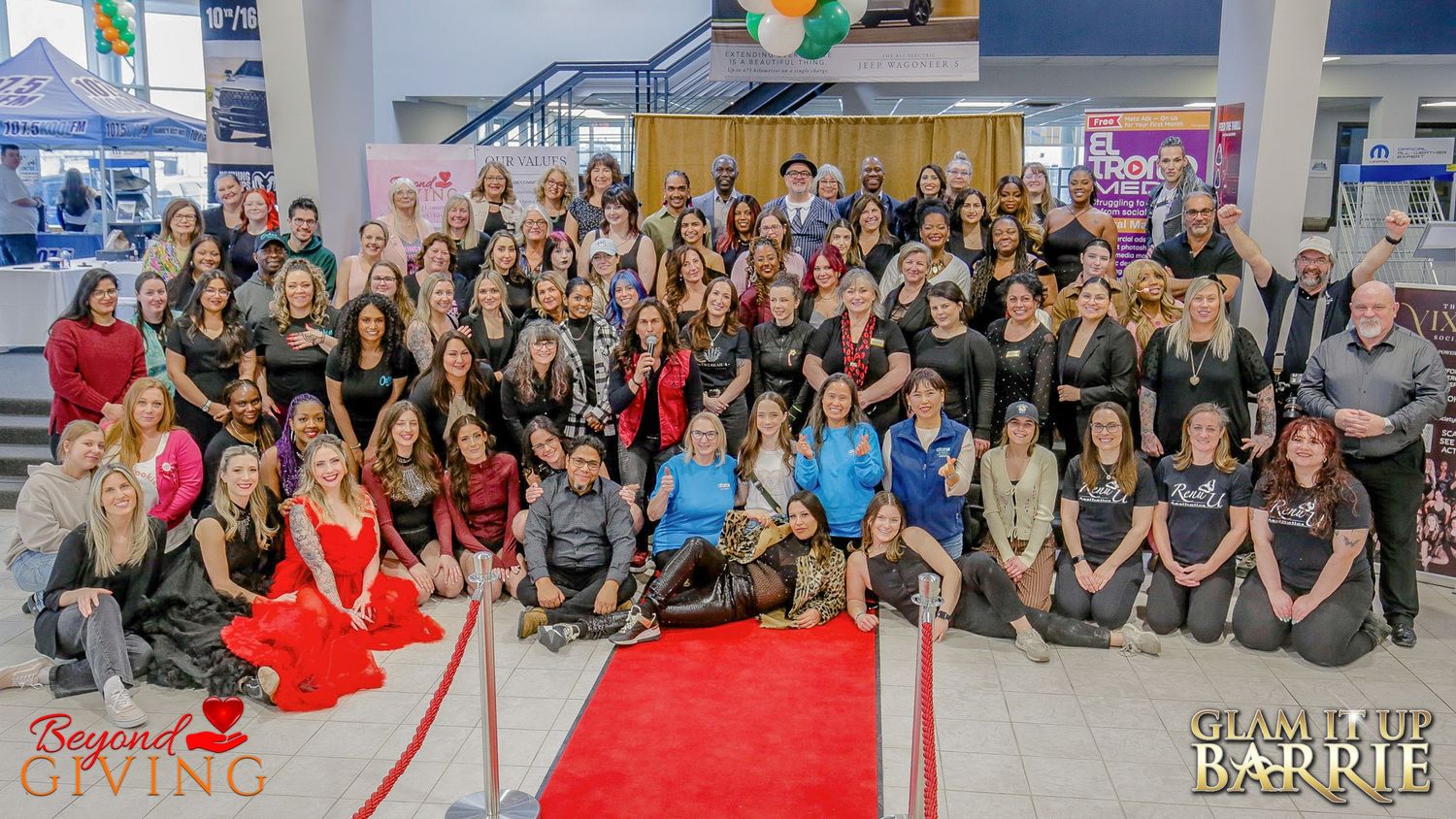 A large group of organizers, stylists, photographers, and volunteers posing together on a red carpet at a Barrie fundraiser.