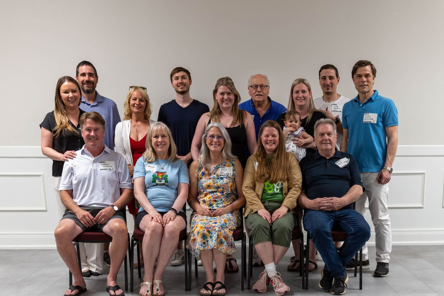 Group photo of smiling adults posing together in two rows inside a bright room with white walls.