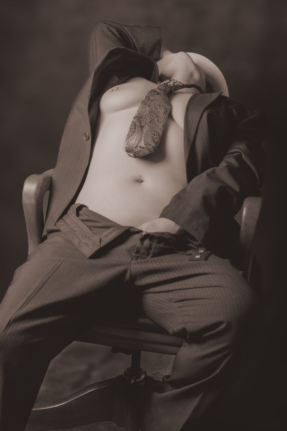 Sepia toned artistic photo of a person in an open suit jacket and loosened tie seated in a chair.