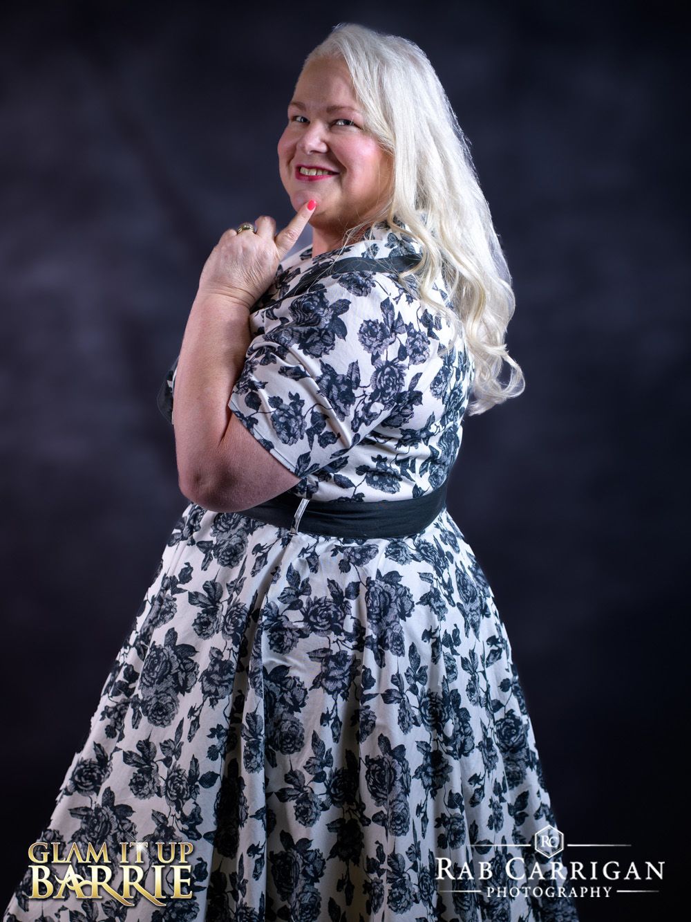 A person wearing a black and white floral print dress poses against a dark background in a glamorous photo shoot.