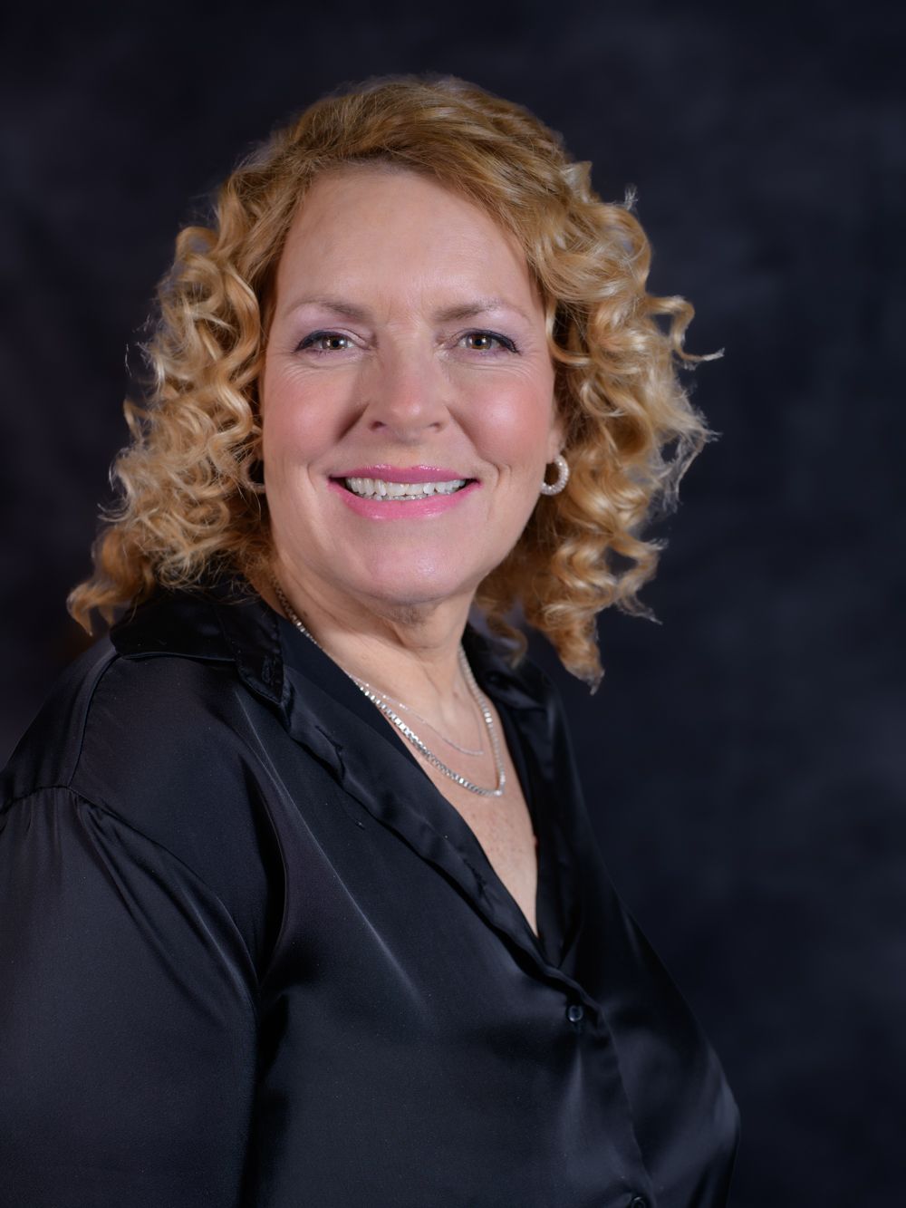 Professional portrait of a smiling woman with curly blonde hair wearing a black blouse.