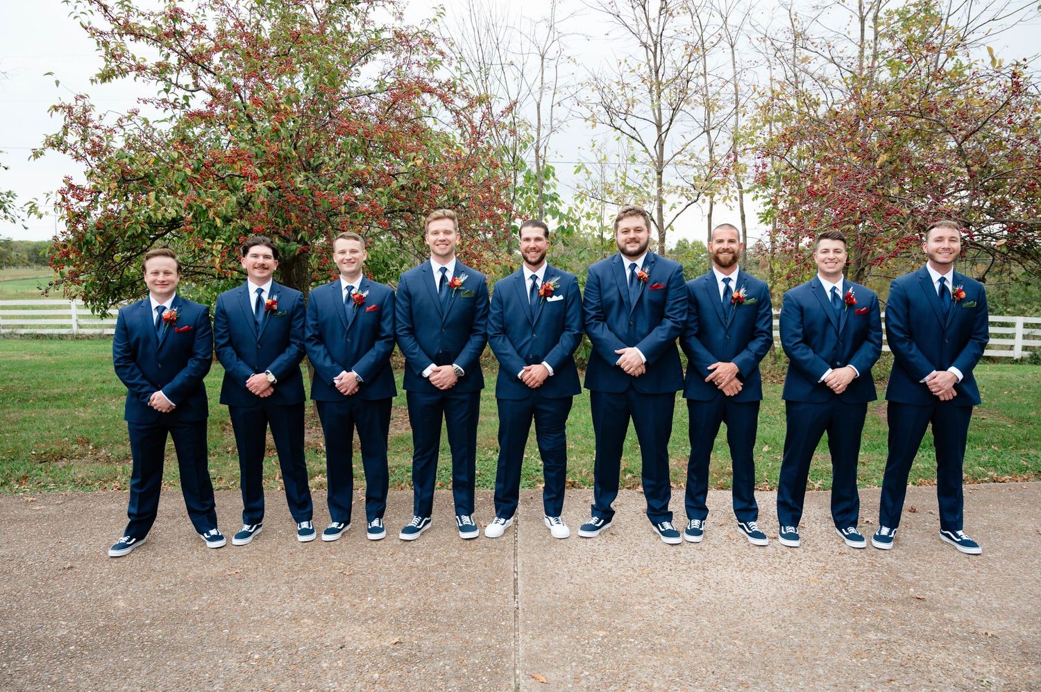 Wedding party in navy suits lined up along fence for formal group photo.
