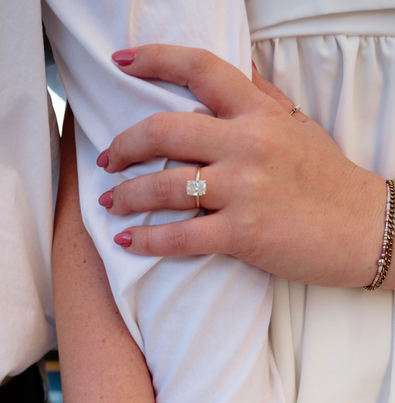 Close-up view of hands wearing wedding rings and red nail polish against white fabric.