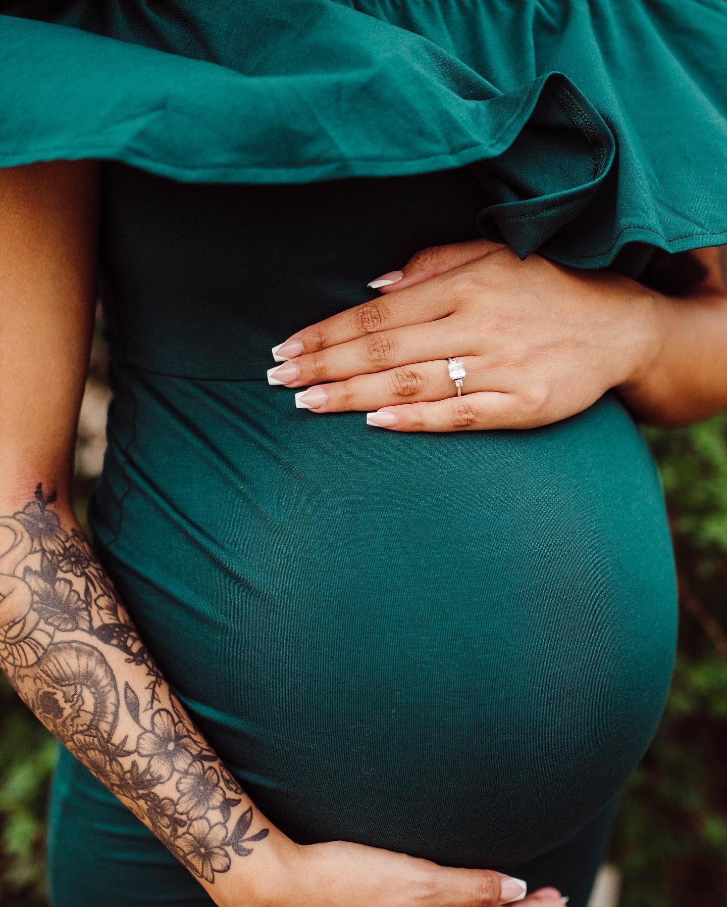 Maternity photo series showing tattooed arm and baby bump in emerald green dress.