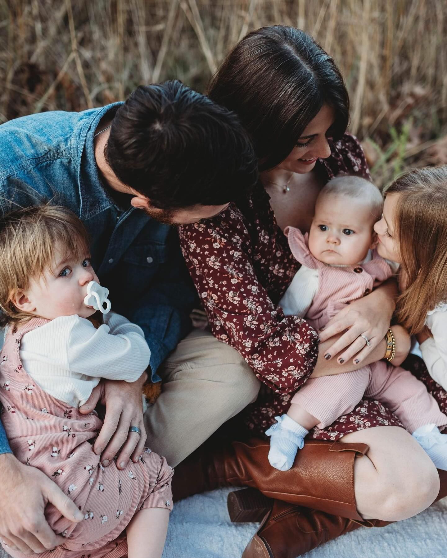 A family cuddles close together while sitting on the ground in casual attire.