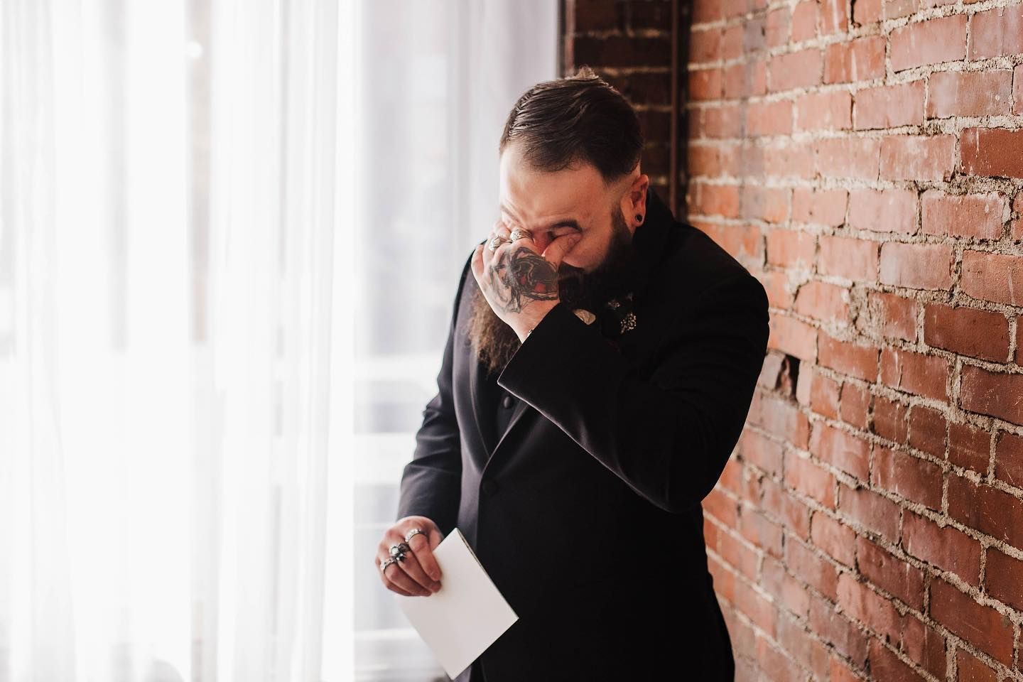 Emotional moment during a wedding ceremony against a rustic brick wall backdrop.