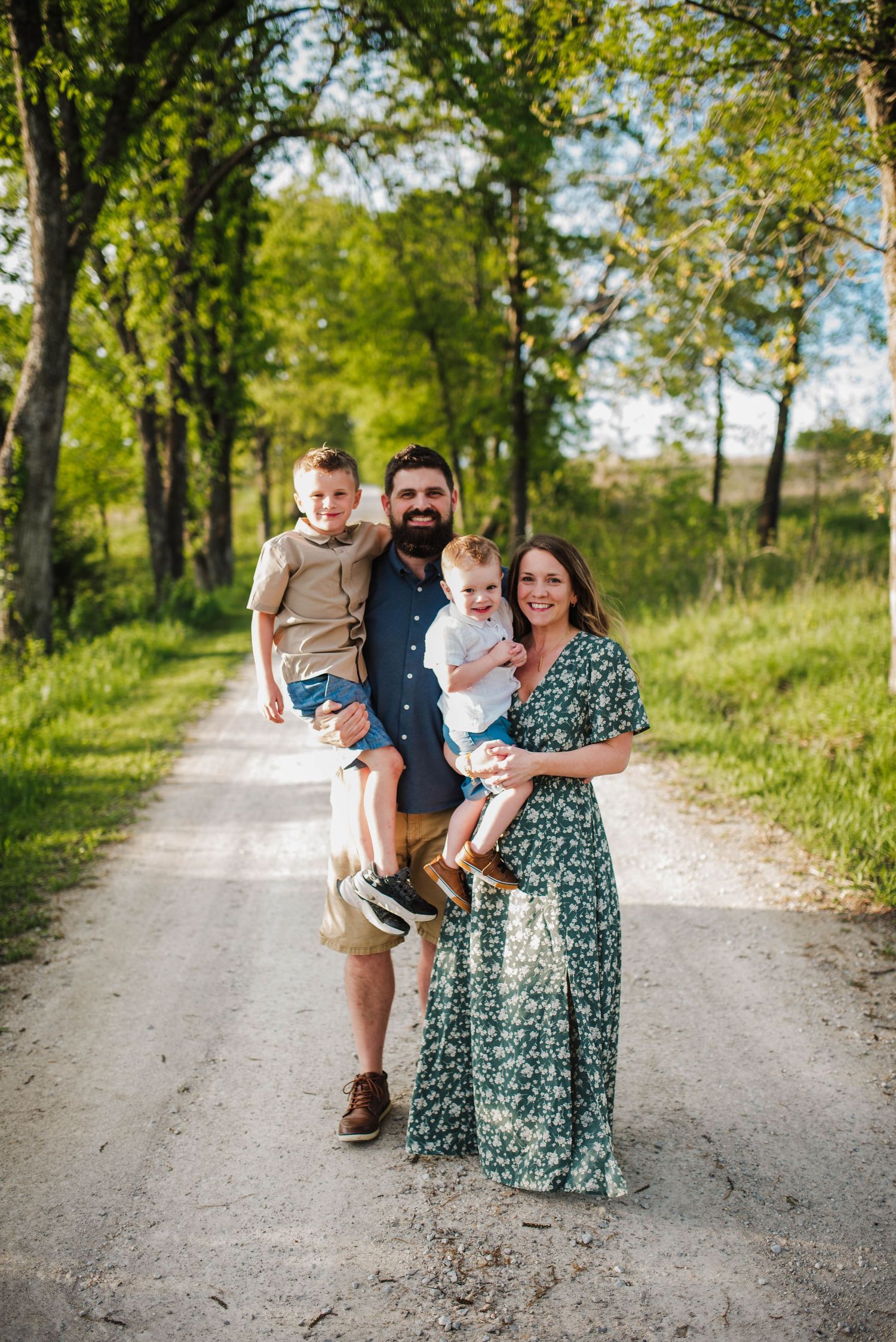 A family poses together on a tree-lined dirt path on a bright summer day.
