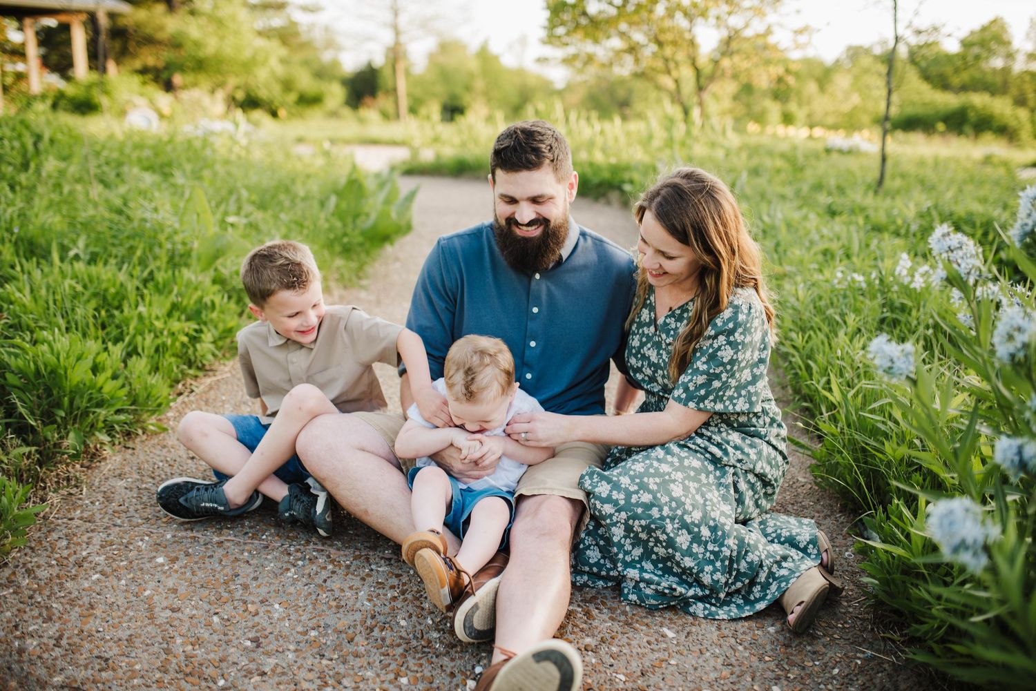 Family relaxing together on grass with flowers during outdoor photo session.
