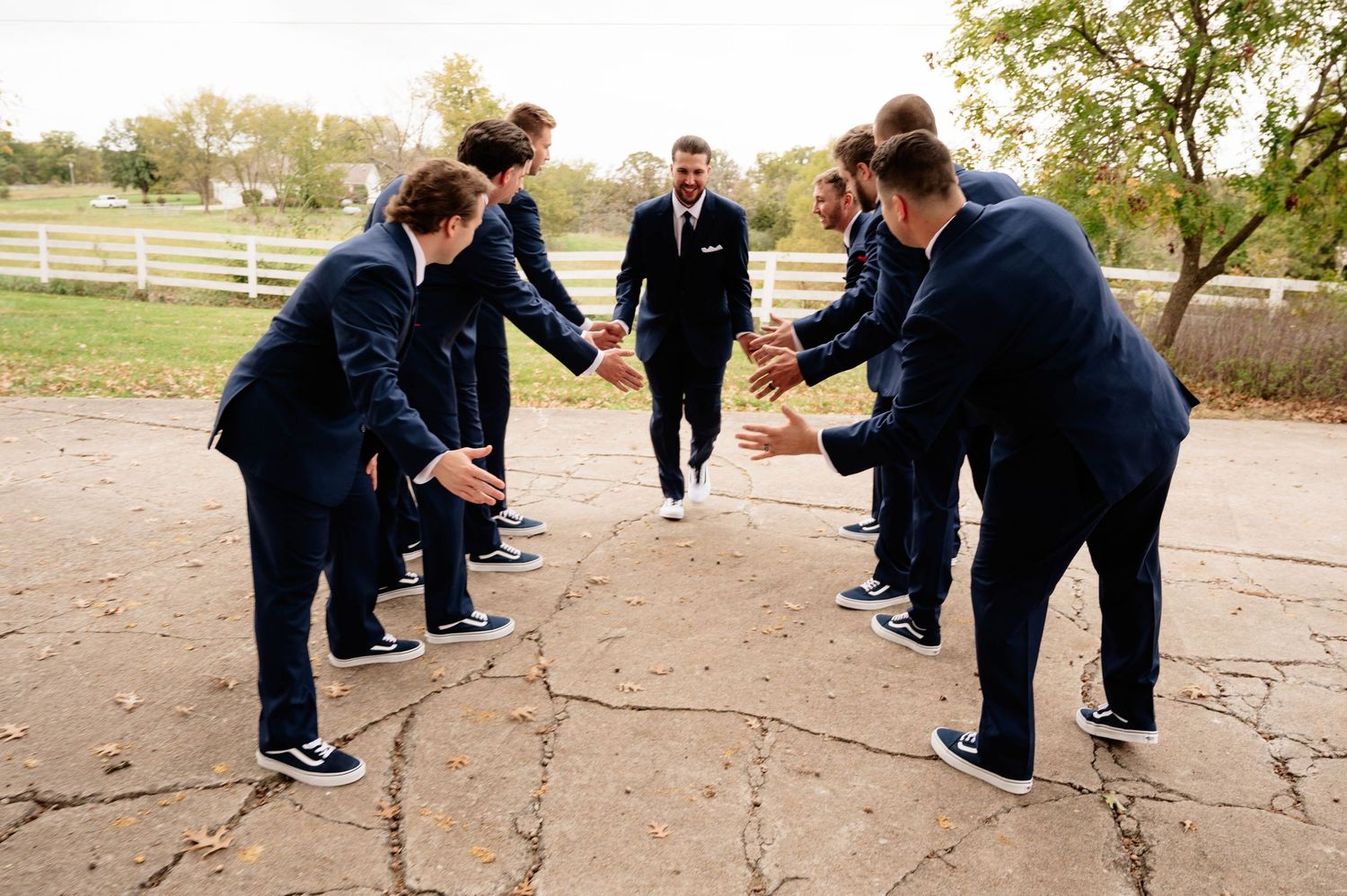 Groomsmen in navy suits playfully jumping in unison outdoors.