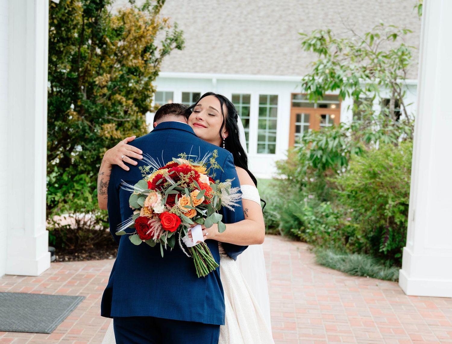 Couple embracing near white pillars with colorful autumn bouquet.