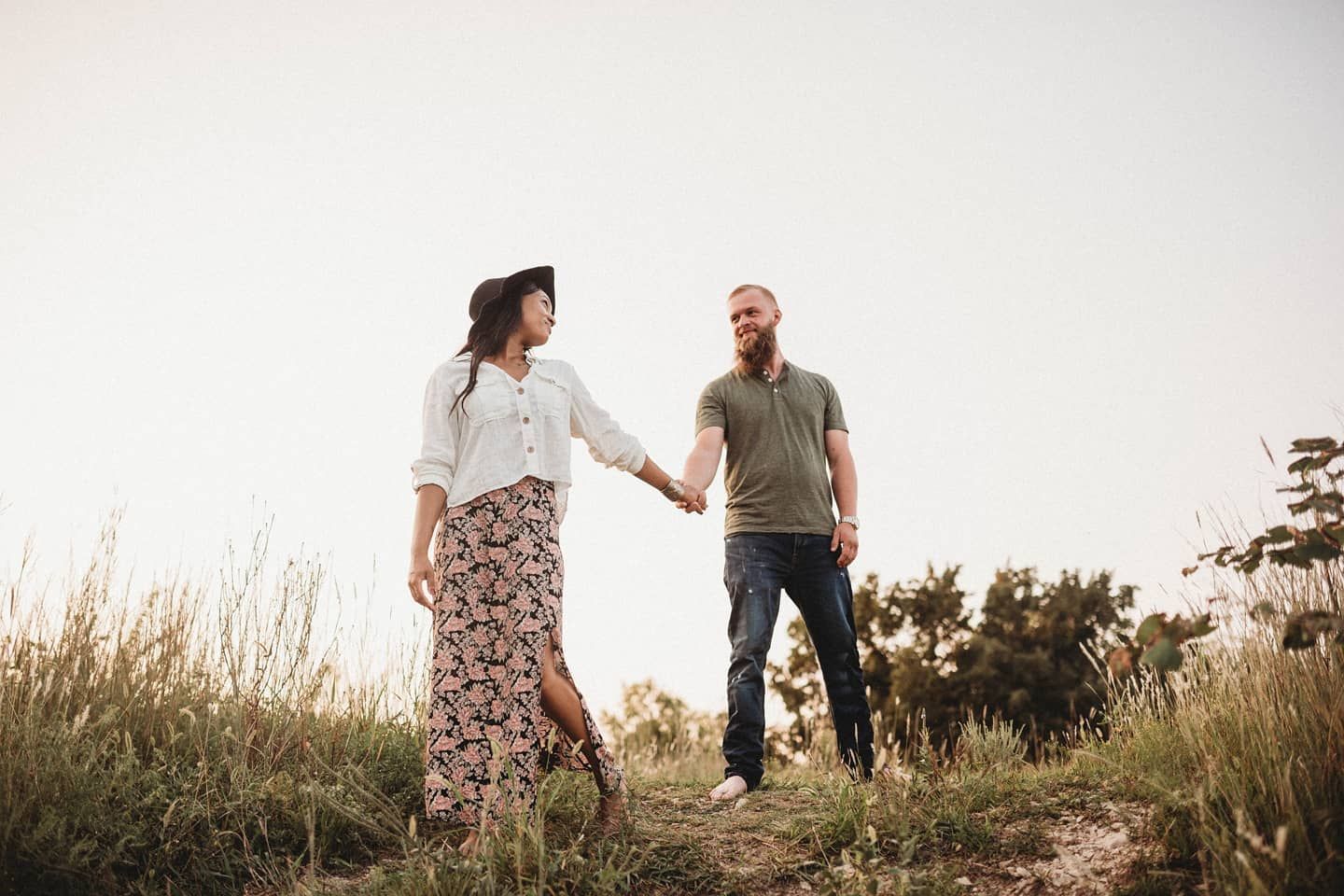 A couple holds hands while standing in tall grass during golden hour.