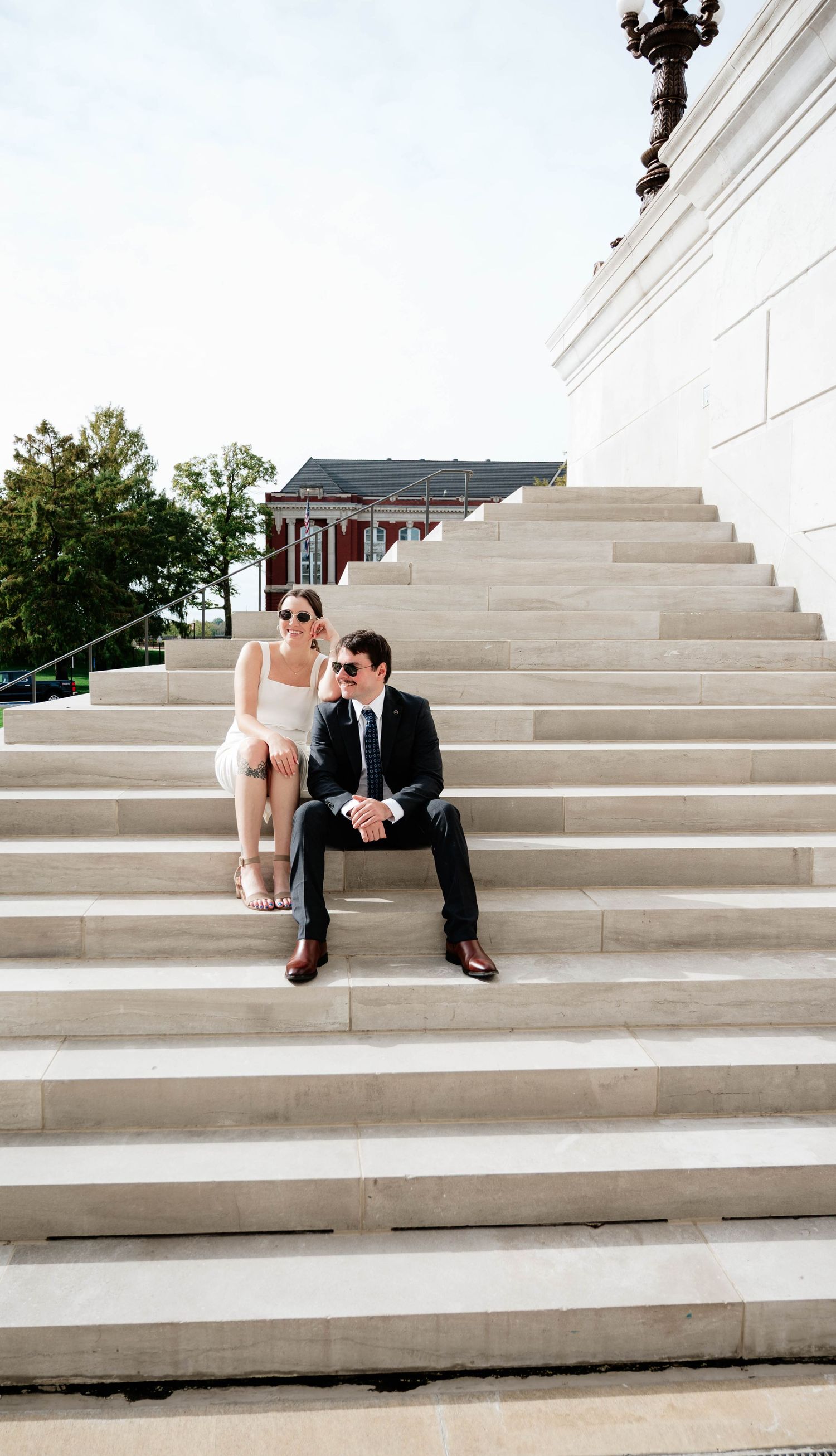 Couple sitting on wide marble steps of a historic building during a photo session.