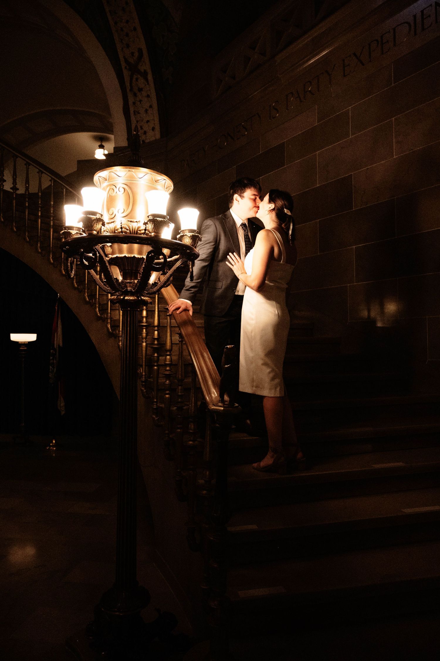 Romantic evening photoshoot in a dimly lit stairwell with vintage lighting.