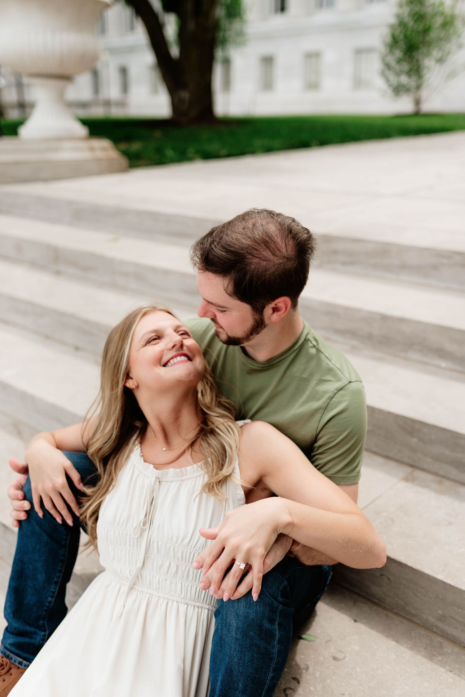 Romantic couple sitting on outdoor steps during a sunny engagement photoshoot.