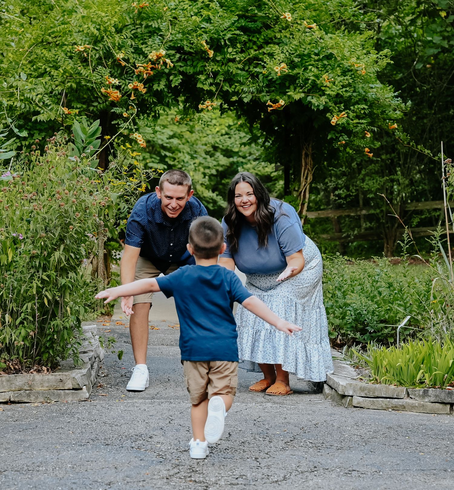 Family plays and poses together on a gravel path in a green garden setting.