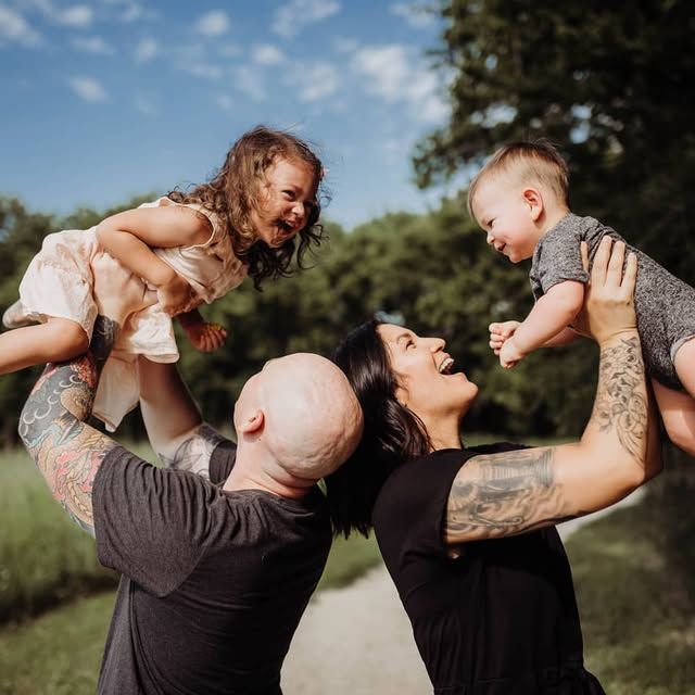 Two adults lift children playfully in the air against a bright blue sky.