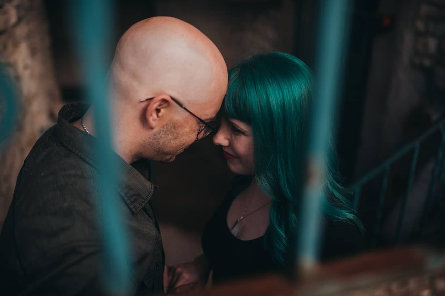 An intimate moment between a couple with vibrant green hair in moody lighting.