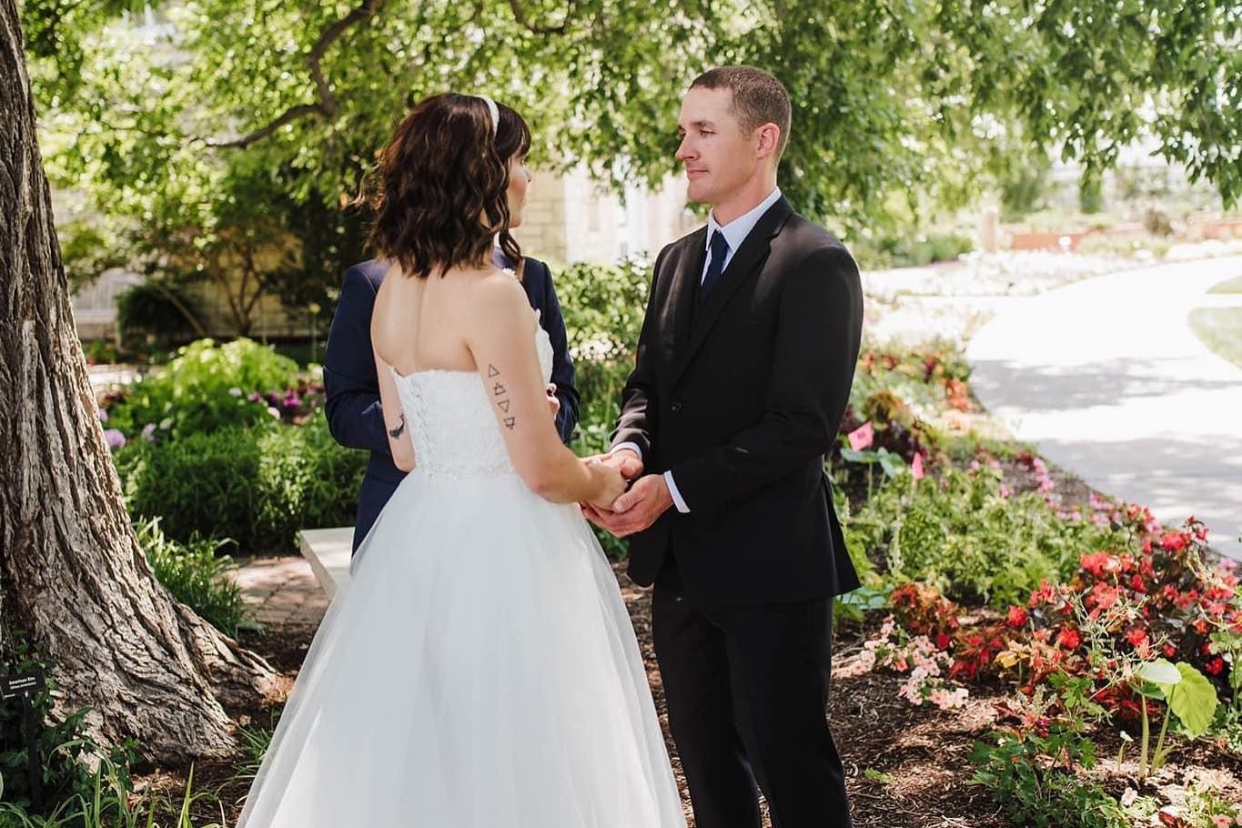 Newlyweds share intimate moments in a garden setting with blooming flowers.