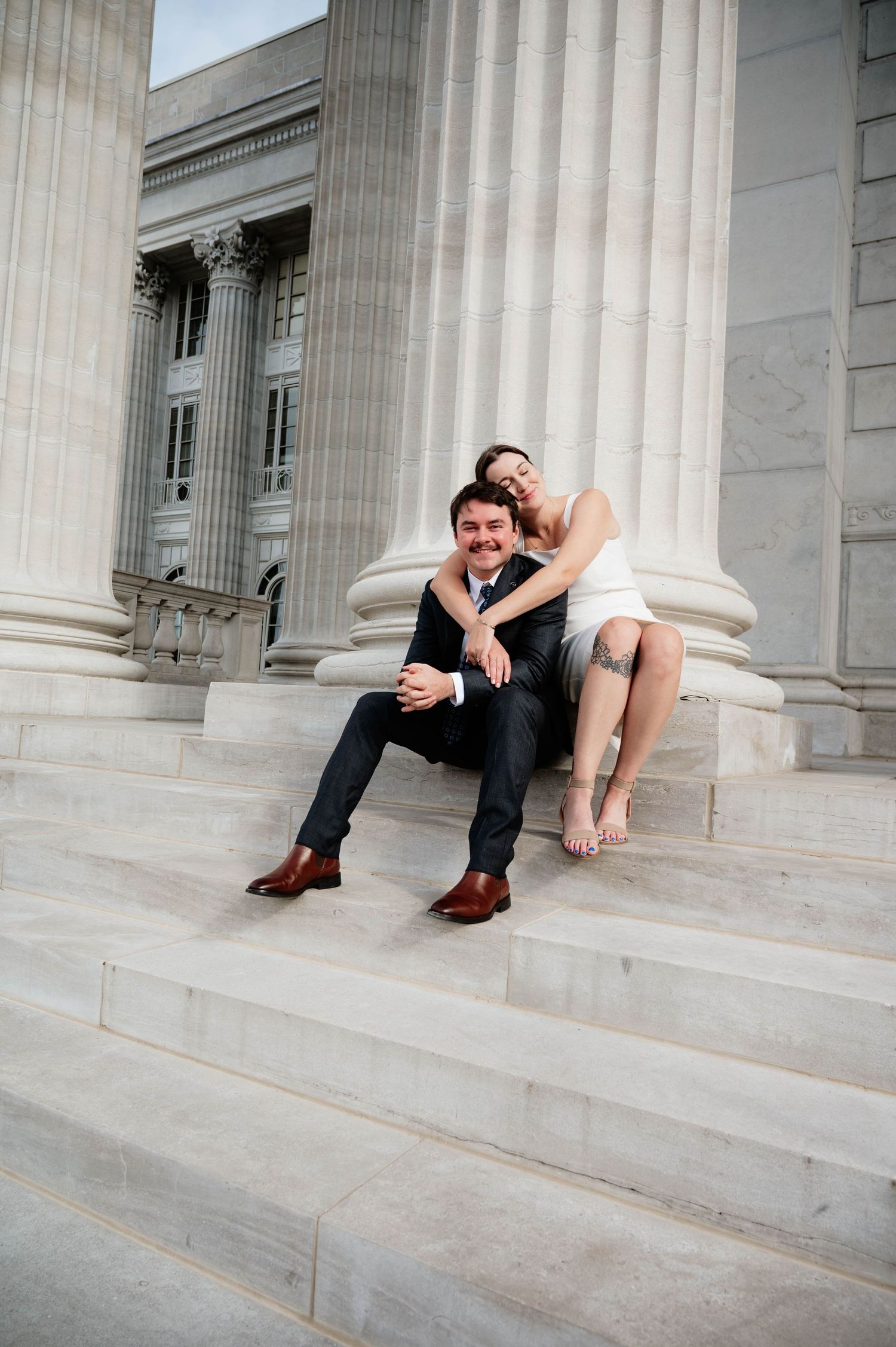 A playful couple shares a moment on the steps of a neoclassical building.