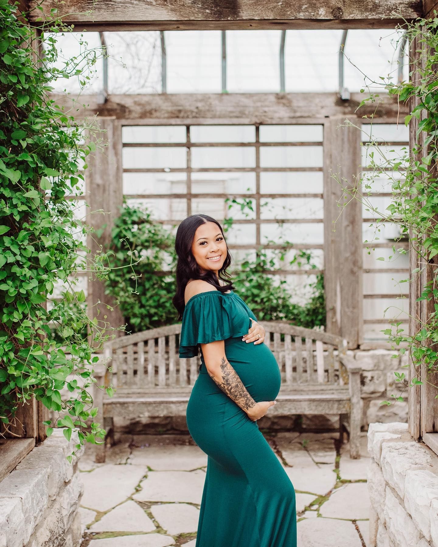 Elegant maternity portraits in emerald dress at rustic greenhouse location.
