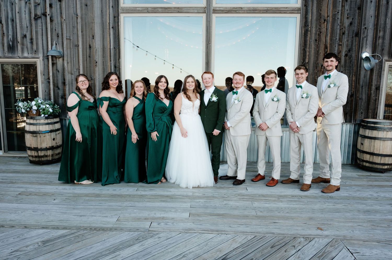 Full wedding party group shot with bridesmaids in green and groomsmen in light gray.