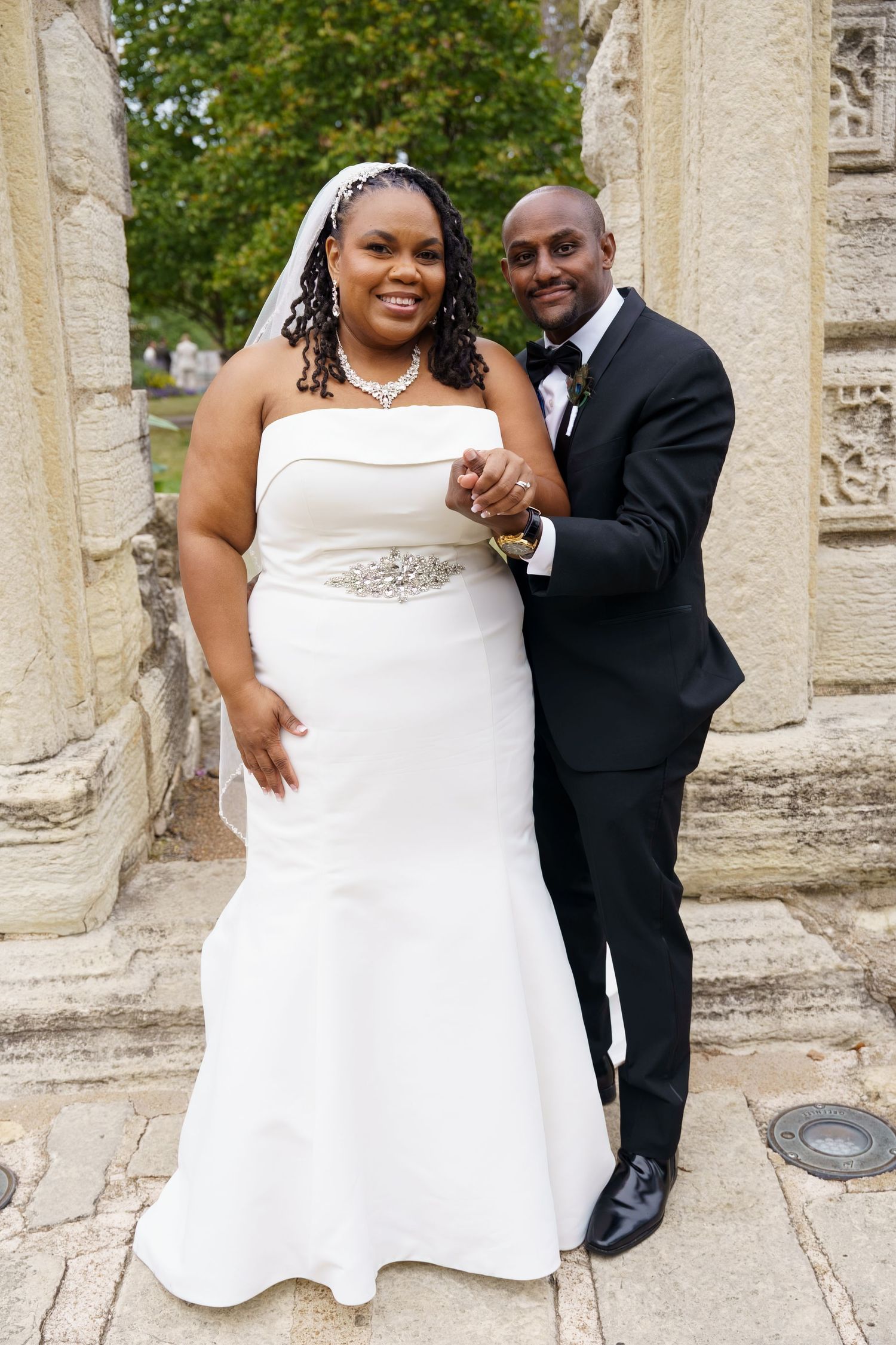 Happy newlyweds share playful moments in front of stone pillars during their wedding photo session.