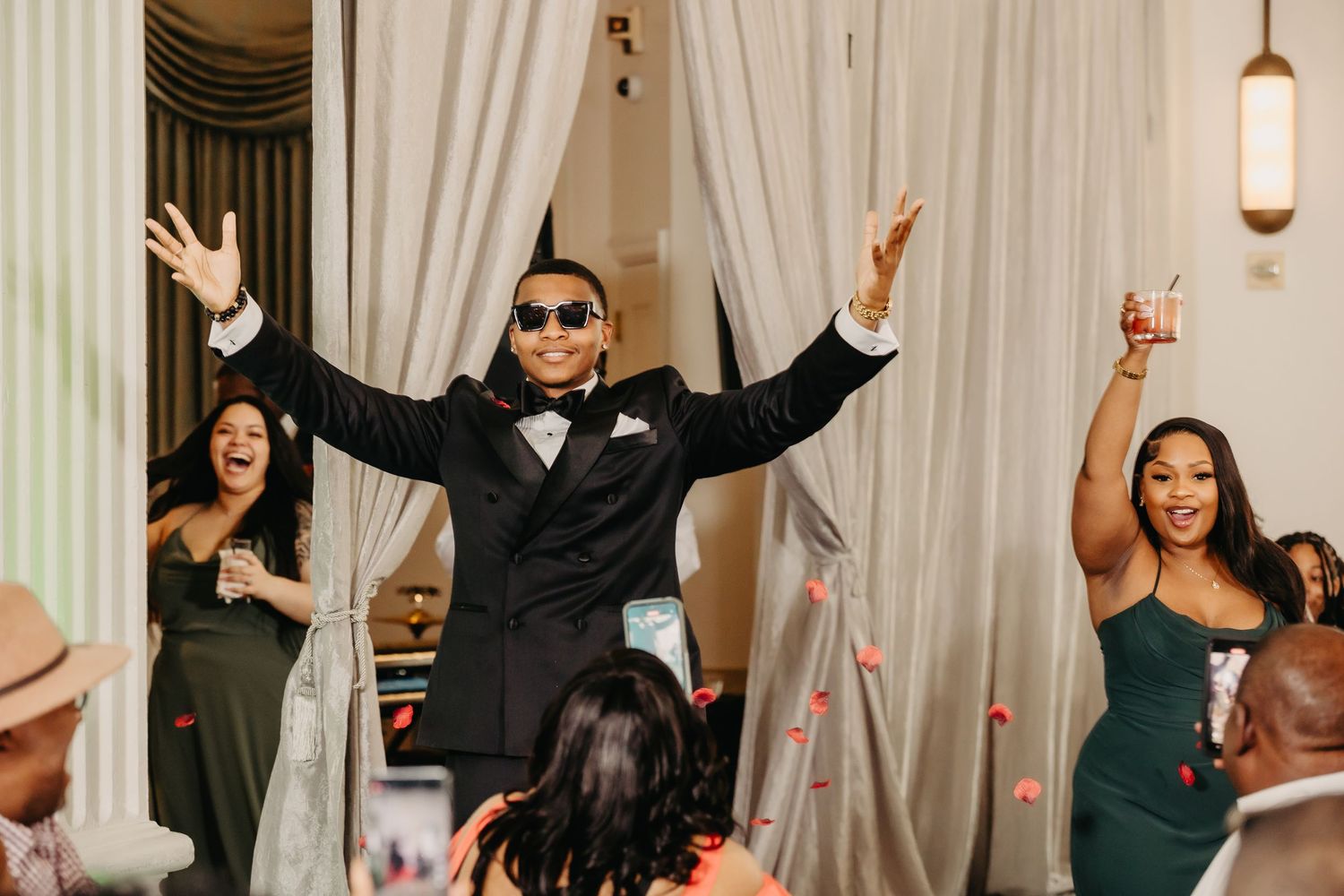 Guests dance energetically during wedding reception in a white-draped venue with pendant lighting.