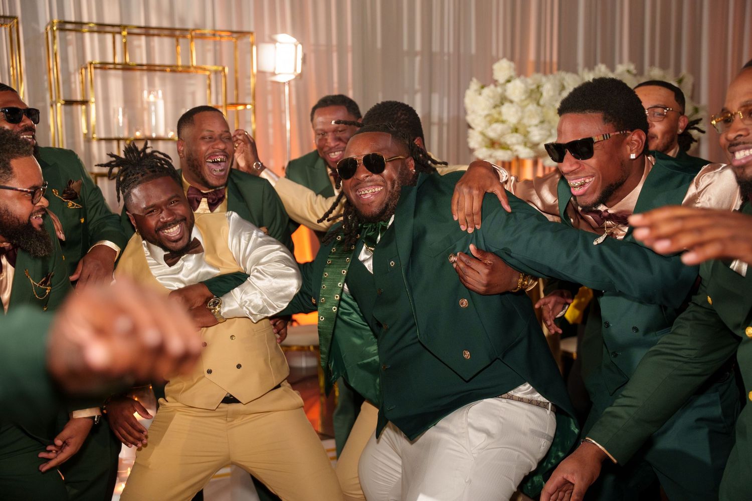 Wedding guests in green jackets dancing enthusiastically at reception celebration.